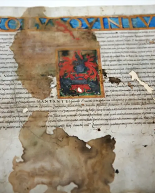 Damaged section of a 16th-century illustrated parchment showing severe stains, discoloration, and text fading