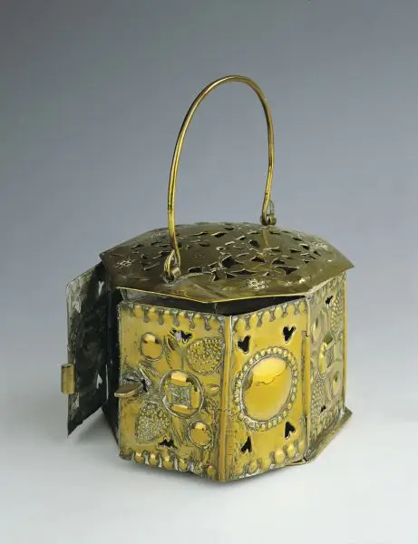 Ornate metal container with a curved handle, pierced lid and an open side door.